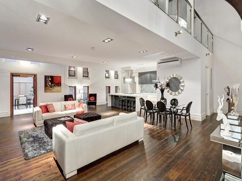 Modern open-concept living and dining area with white sofas, dark wood floors, dining table with black chairs, kitchen island, wall art, and decorative elements. Bright, spacious, and elegantly furnished.